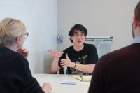 a man sitting at a table speaking to a woman and a man gestures while speaking